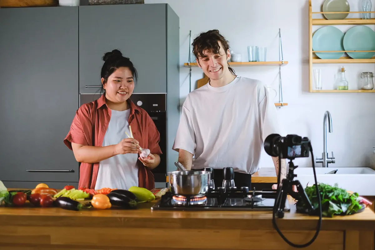 Two vloggers cooking and filming culinary content in a stylish kitchen setup.