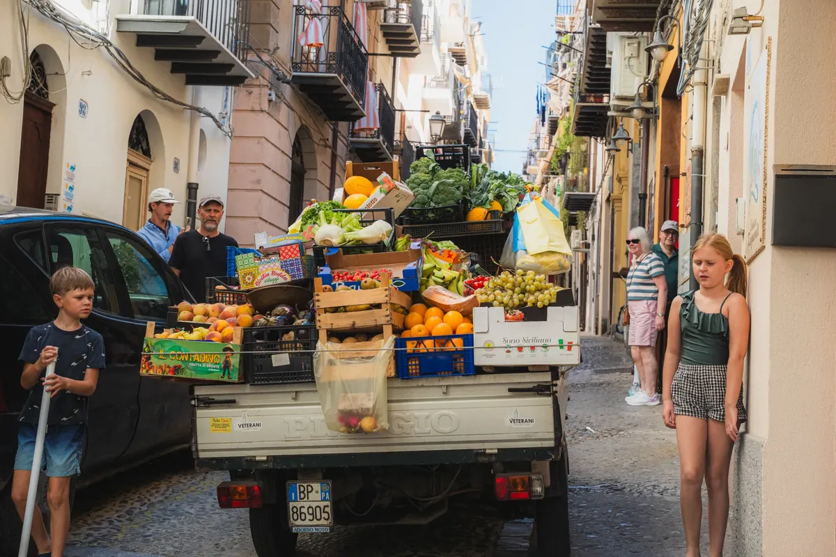 Vibrant street market scene showing a truck loaded with fresh fruits and vegetables on an Italian street.